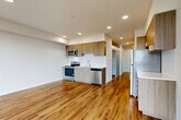 This well-appointed one-bedroom, one-bathroom unit at 2721 Wetmore Ave in Everett, WA offers a thoughtfully designed layout across a single floor. The open-concept living area seamlessly combines the dining room, kitchen, and living space, creating a bright and functional environment. Warm hardwood-style flooring runs throughout, complementing the clean, modern aesthetic. The kitchen is equipped with stainless steel appliances—including a refrigerator, electric range, microwave, and dishwasher—alongside light wood cabinetry, white quartz countertops, and a subway tile backsplash. A hallway lined with two closets provides generous storage and leads to the bedroom, which receives excellent natural light through large windows with views of the surrounding urban landscape. The bathroom features a long wood-toned vanity with a white countertop, a full-width mirror, and consistent hardwood-style flooring. Recessed lighting throughout adds to the clean, contemporary feel. A private balcony accessible from the living area extends the living space outdoors and offers additional city views. The unit presents a cohesive modern design with practical finishes suited for everyday living.
