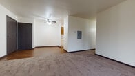 This single-floor unit at 1240 Emerald Terr in Sun Prairie, Wisconsin, offers a straightforward, functional layout with a mix of carpet and hardwood-style vinyl flooring throughout. The open living area is finished with neutral white walls, dark baseboards, and a ceiling fan with integrated lighting, creating a clean and practical atmosphere. An electrical panel is conveniently accessible from the main living space. The living room transitions seamlessly toward a dedicated area featuring a sliding glass door that allows natural light to enter and provides views of the surrounding greenery outside.

The galley-style kitchen is equipped with warm oak cabinetry, light countertops, a built-in sink, and a full-size refrigerator, all set atop durable hardwood-style vinyl flooring. Baseboard heating units are present throughout, ensuring efficient warmth during Wisconsin winters.

The bedroom offers a comfortable, carpeted space with a natural window that brings in outside light, a closet with visible shelving, and a baseboard heater. The full bathroom features a white tile surround tub-and-shower combination, a wood-toned vanity with countertop, and distinctive mosaic-style floor tile that adds visual interest to the otherwise clean, minimal space.