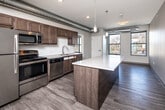 Located at 3201 Forest Ave in Des Moines, Iowa, this thoughtfully designed 3-bedroom, 2-bathroom unit offers a compelling blend of modern finishes and industrial character across a single floor. The open-concept kitchen serves as the heart of the space, featuring rich warm-toned cabinetry, a white subway tile backsplash, stainless steel appliances including a gas range, microwave, dishwasher, and refrigerator, and a central island with a light quartz countertop. Exposed metallic ductwork runs overhead throughout the living and kitchen areas, lending an urban, loft-inspired aesthetic. Pendant lighting above the island and recessed ceiling lights add both ambiance and practicality. Light hardwood-style flooring flows through the main living areas, while plush carpet provides comfort in all three bedrooms. Each bedroom benefits from natural light through generously sized windows with neighborhood views. The primary bedroom is a comfortable size and connects to a well-appointed closet with wire shelving. Additional bedrooms include built-in closet storage. Both bathrooms are finished with dark wood vanities, quartz countertops, and tub-shower combinations. An in-unit washer and dryer area adds everyday convenience, completing this well-rounded and move-in-ready home.