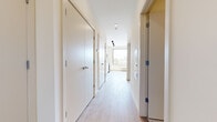 Located at 269 Orange Street in New Haven, CT, this efficiently designed single-floor unit offers a clean, contemporary layout making smart use of its compact footprint. The open-plan kitchen and living area serves as the heart of the space, featuring light wood-tone flooring, recessed lighting, and a large black-framed window that floods the room with natural light and provides views of the surrounding New Haven cityscape. The kitchen is equipped with white cabinetry, stainless steel appliances including a refrigerator and dishwasher, and a white electric range with an over-the-range microwave — all contributing to a sleek, functional aesthetic. The hallway runs the length of the unit, lined with multiple white flush-panel doors providing access to storage and key rooms, and is illuminated by recessed ceiling lights that maintain the bright, airy feel throughout. The bathroom is finished with neutral stone-patterned tile flooring, a walk-in shower with white subway tile surround, a white vanity, and clean modern fixtures. Crisp white walls and consistent light wood flooring unify the entire space, creating a cohesive, minimalist atmosphere well-suited to urban living in the heart of New Haven.
