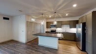 Located at 6004 Grandover Village Rd in Greensboro, NC, this single-floor residence offers a thoughtfully designed layout with modern finishes throughout. The open-concept kitchen is a standout feature, showcasing rich taupe cabinetry, dark granite countertops, a white subway tile backsplash, and a full suite of stainless steel appliances. A central island with pendant lighting adds both function and style, while hardwood-style flooring flows seamlessly through the kitchen and living areas. The living room is bright and spacious, with natural light from large windows and a glass door leading to an outdoor balcony. Bedrooms are carpeted for comfort and include a ceiling fan in one room and built-in shelving in another, offering convenient storage solutions. A walk-in closet with wire shelving provides generous storage. The primary bathroom features a dual-sink vanity with marble-style countertops, dark cabinetry, a large mirror, and tile flooring. A secondary bathroom includes a single vanity with matching finishes and a tub-shower combination. The overall aesthetic is clean and contemporary, with neutral tones and quality materials creating a polished, move-in-ready atmosphere.