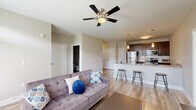 Located at 3483 Apollo Ln in West Lafayette, Indiana, this well-appointed 2-bedroom, 2-bathroom unit offers a thoughtfully designed single-level layout. The open-concept living and kitchen area serves as the heart of the home, anchored by a large granite-topped island with bar seating and elegant pendant lighting overhead. The kitchen is equipped with rich dark-brown cabinetry, a white subway tile backsplash, and a full suite of stainless steel appliances. Wood-style flooring flows throughout the main living areas, complementing the neutral warm-gray color palette. The living room is bright and inviting, featuring a ceiling fan and a glass door that lets in natural light and provides outdoor access. Both bedrooms are carpeted for comfort and include closets with wire shelving systems for organized storage. The primary bedroom connects directly to its own bathroom, which features a dark-wood vanity with a granite countertop, a framed mirror, and modern light fixtures. The second bedroom is bright with a large window overlooking the exterior. A dedicated laundry area with a full-size washer is also included within the unit, adding convenience to this move-in-ready home.