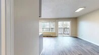 Located at 3050 SW 10th Ave in Portland, Oregon, this single-floor unit offers a thoughtfully laid-out living space with consistent wood-look flooring throughout. The open living area is bathed in natural light from a wide bank of windows and a sliding glass door that leads to a private balcony overlooking lush, tree-lined surroundings — an inviting feature that brings the outdoors in. A textured ceiling and baseboard heating complete the comfortable living environment.

The kitchen is well-appointed with ample grey cabinetry providing generous storage, stainless steel appliances including an electric range and refrigerator, a under-cabinet range hood, and a double-basin sink with a window view to the greenery outside. The layout allows for efficient meal preparation and easy flow between the kitchen and living areas.

The bedroom is a serene retreat, featuring neutral walls, wood-look flooring, and a set of mirrored sliding closet doors that enhance the sense of space while offering practical built-in storage with shelving and hanging space.

The bathroom is clean and functional, finished with wood-look flooring, a full tub-shower combination, and classic white fixtures. This unit presents a comfortable and practical living space in a verdant Portland neighborhood.