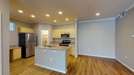 This single-floor residence offers a thoughtfully designed layout that combines functionality with comfortable living. The open-concept kitchen serves as the centerpiece of the home, featuring light-toned cabinetry, granite-look countertops, and a full suite of stainless steel appliances including a refrigerator, electric range, microwave, and dishwasher. A central kitchen island with a double sink provides additional prep space and casual dining potential. A dedicated walk-in pantry offers generous storage, while warm wood-look flooring flows throughout the main living areas, adding a cohesive and inviting feel.

The spacious living room benefits from crown molding, recessed lighting, and a ceiling fan, with a sliding glass door that opens to a private balcony overlooking lush greenery. The bedrooms are carpeted for comfort, each equipped with ceiling fans and ample natural light from windows with vertical blinds. The bathroom is finished with granite-look countertops, light wood cabinetry, a full-size mirror, and a shower-tub combination.

A dedicated in-unit laundry area houses a full-size washer and dryer side by side, adding everyday convenience. Neutral gray walls and clean white trim throughout lend the space a modern, move-in-ready aesthetic.