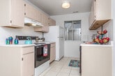 Located at 44825 Mound Rd in Sterling Heights, Michigan, this single-floor unit offers a practical and comfortable layout designed for everyday living. The galley-style kitchen is efficiently arranged with light wood cabinetry lining both walls, white laminate countertops, a smooth-top electric range, dishwasher, and a window at the far end that allows natural light to brighten the space. Light ceramic tile flooring runs throughout the kitchen, complementing its clean, functional design. The open living area features neutral carpeting and a pendant light fixture, creating a welcoming atmosphere with a clear sightline to the entry and adjacent rooms. The bedroom is generously sized with plush carpet, vertical blinds on the window, and a built-in closet with bifold doors, providing ample storage. Additional storage is available via open shelving visible near the laundry area. The full bathroom is finished with ceramic tile flooring, a tub-shower combination with white tile surround, a single vanity with a broad mirror, and a ceiling vent for ventilation. A dedicated in-unit laundry space houses a full-sized top-load washer and dryer side by side, with overhead shelving for added storage convenience. The overall layout is straightforward and well-maintained, offering essential amenities in a compact, single-level footprint.