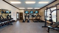 This fitness center at 500–576 Noel Ln in Smyrna, Tennessee, offers a well-equipped, single-floor workout facility designed to support a wide range of exercise routines. The space features durable speckled rubber flooring throughout, providing both safety and comfort during workouts. Crown molding and neutral-toned walls give the room a clean, polished aesthetic.

The cardio section is outfitted with multiple treadmills and elliptical machines, each positioned in front of ceiling-mounted flat-screen TVs, allowing users to stay entertained during their sessions. A large wall mirror expands the sense of space and aids in form monitoring. Natural light filters in through windows that overlook an outdoor area, adding a bright and open ambiance to the room.

The strength training area includes a multi-functional cable machine, a Smith machine with an adjustable bench, a rack of dumbbells ranging across various weights, kettlebells, medicine balls, a stability ball, and a spin bike — providing comprehensive options for resistance and functional training. A motivational wall graphic reading "Stay Humble, Hustle Hard" adds energy to the environment.

The facility is brightly illuminated by recessed panel lighting and is accessible via dark-framed glass doors. Signage for fitness center rules is posted near the entrance, and the space maintains a tidy, organized layout throughout.