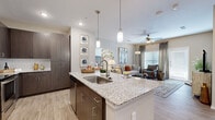 Located at 15630 Walden Rd in Montgomery, TX, this single-floor residence offers a thoughtfully designed open-concept layout that seamlessly connects the kitchen, dining, and living areas. The kitchen serves as the heart of the home, showcasing a large granite-topped island with an undermount sink and seating, dark espresso cabinetry, stainless steel appliances, a classic subway tile backsplash, and stylish pendant lighting overhead. Light wood-style flooring flows throughout, enhancing the bright and airy feel of the space. The living room is generously sized, filled with natural light from multiple windows dressed with blinds and drape panels, and features a ceiling fan overhead. The bedrooms are comfortably sized, each with ample natural light and well-appointed finishes. The bathrooms continue the home's design language with granite countertops, dark wood cabinetry, large mirrors, and wood-style flooring — one bathroom features a walk-in glass-enclosed shower. A dedicated laundry area is also present within the unit. Overall, the residence offers a clean, contemporary aesthetic with warm, neutral tones that create an inviting and functional living environment.