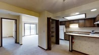 This single-floor residence offers a practical and functional layout designed to maximize everyday comfort. The kitchen is equipped with dark wood cabinetry, a white refrigerator, a sink with counter space, and a breakfast bar that provides a natural transition between the kitchen and the living area. Tile flooring in the kitchen adds durability, while a textured ceiling runs throughout the space, adding a classic character overhead. A built-in storage closet with shelving is conveniently situated between the kitchen and living areas, offering ample organizational space. The carpeted living area is open and airy, benefiting from natural light that streams in through a large sliding glass door that opens to a private balcony, providing an outdoor retreat. The soft, neutral wall tones throughout the space create a clean and understated aesthetic. The overall layout flows cohesively from the kitchen to the living area, making the space feel connected and easy to navigate. The combination of functional storage, defined zones, and access to outdoor space makes this a well-rounded and practical residence.