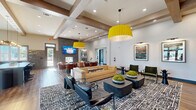 Located at 3145 Prado Ln in Charlotte, NC, this expansive single-floor amenity facility offers a thoughtfully designed collection of spaces built for comfort, recreation, and community. The welcoming lounge area makes an immediate impression with its soaring ceilings adorned with exposed wood beam detailing, bold yellow pendant lighting, rich hardwood floors, and a full built-in shelving wall with integrated media display. Curated furnishings, patterned area rugs, and framed artwork contribute to a polished yet inviting atmosphere. A communal kitchen nearby features sage green cabinetry with brass hardware, a dramatic textured brick backsplash, a large center island, stainless steel appliances, and an artisan globe pendant light cluster — ideal for gatherings and events. The fitness center is generously sized, flooded with natural light through large windows, and outfitted with a comprehensive range of cardio and strength equipment, ceiling fans, and wall-mounted displays. An adjoining functional training room provides space for dedicated workout routines with outdoor views. The golf simulator room, finished in dark tones with turf flooring and a ceiling-mounted projector, offers an immersive experience. The game room rounds out the amenities with a billiards table, lounge seating, wainscoting detail, and a wall-mounted TV — perfect for relaxed socializing.