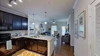 This single-floor residence offers a thoughtfully designed open-concept layout that seamlessly connects the kitchen, dining, and living areas. The kitchen is a standout feature, anchored by a generous granite-topped island with seating, dark espresso cabinetry, stainless steel appliances, and stylish pendant lighting that adds warmth and visual interest overhead. Crown molding runs throughout the main living area, adding a refined architectural detail to the space.

The living room is bright and inviting, benefiting from natural light streaming through multiple windows fitted with blinds and curtains. A ceiling fan provides comfort, while rich hardwood-style flooring runs consistently across the main areas, tying the open floor plan together cohesively.

The bedroom is a serene retreat, featuring a ceiling fan, large windows that allow ample natural light, and hardwood-style flooring. A spacious walk-in closet with multi-tier wire shelving provides generous storage capacity.

The bathroom is well-finished with dark cabinetry, a granite vanity countertop, tile-surround tub and shower combination, and coordinating hardwood-style flooring. Overall, the space balances modern finishes with a warm, livable ambiance suitable for comfortable everyday living.