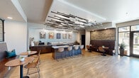 Located at 2445 Estrella Parkway in Goodyear, AZ, this single-floor community amenity space offers a generously sized, open-concept layout designed for socializing and recreation. The space is unified by warm light wood flooring throughout and transitions seamlessly between distinct functional zones.

The main lounge area is anchored by a striking embossed metallic tile ceiling that adds an industrial-chic character, complemented by ambient LED cove lighting. Comfortable leather seating, a built-in media wall with multiple flat-screen TVs, and open shelving with curated décor define this gathering space. A cozy fireplace and stone accent wall add warmth and texture to the atmosphere.

The game room zone features a full-size pool table, foosball table, and additional lounge seating, making it a lively hub for entertainment. Adjacent to this, a well-appointed kitchen bar area showcases a bold, one-of-a-kind ceiling installation composed of baseball bats, nodding to the region's sports culture. Dark wood cabinetry, a large island with bar seating, and full counter service equipment complete this social kitchen.

The entry foyer welcomes visitors with floor-to-ceiling glass doors that flood the space with natural light and offer views to an outdoor patio. Throughout, sports-themed artwork and thoughtful design details contribute to a cohesive, dynamic ambiance suited for community gatherings.