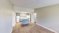 Located at 600 Weakley Ln in Smyrna, Tennessee, this two-bedroom, two-bathroom single-floor residence offers a functional and well-organized layout. The combined kitchen and living area serves as the heart of the home, featuring durable wood-look flooring, neutral toned walls, and a large window that fills the space with natural light and provides outdoor views. The kitchen is equipped with gray cabinetry, light stone-patterned countertops, white appliances including a refrigerator, range, and dishwasher, a stainless steel sink, and a central island with matching countertop — ideal for meal prep and casual dining. The living area offers a clean, open feel with a textured ceiling and easy access to the front entry. Both bedrooms are carpeted and finished with the same neutral palette and textured ceilings. The spacious primary bedroom includes a ceiling fan, a window overlooking greenery, and two louvered bi-fold closets with direct access to its en-suite bathroom, which features gray cabinetry, a white countertop, and a tub-shower combination. The second bathroom mirrors this design with wood-look flooring. A dedicated utility room and hallway complete the practical floor plan.
