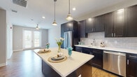 This single-floor residence showcases a contemporary design with thoughtfully selected finishes throughout. The kitchen serves as a central highlight, featuring rich dark espresso cabinetry extending to the ceiling for ample storage, paired with crisp white quartz countertops and a neutral gray subway tile backsplash. A spacious central island provides additional prep and dining space, illuminated by stylish pendant lights overhead. Stainless steel appliances, including a French door refrigerator, gas range, built-in microwave, and dishwasher, complete the well-appointed space. Warm hardwood-style flooring runs throughout the main living areas, lending a cohesive and inviting feel.

The living area benefits from natural light and direct access to a private balcony through glass-paneled doors, offering pleasant outdoor views. Bedrooms feature plush carpeting, ceiling fans, and large windows that invite natural light. The bathroom is finished with dark-framed cabinetry, a white quartz vanity top, an undermount sink, and a framed mirror, maintaining the unit's consistent modern aesthetic. Neutral wall tones and clean architectural lines throughout create a bright, functional, and stylish living environment.