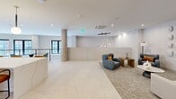 Located at 968 Bonnel Ct in Union, NJ, this thoughtfully designed single-floor space offers a sophisticated, contemporary aesthetic throughout its generously proportioned open layout. The interior is defined by a seamless flow between multiple functional zones, unified by light-toned stone-look flooring, recessed lighting, and a crisp white ceiling palette.

The central gathering area features a large waterfall-edge marble island flanked by leather-upholstered barstools, set beneath a row of globe pendant lights with brass hardware. Behind the island, warm wood cabinetry, a textured stone accent wall, wall-mounted display, and built-in beverage storage create a polished, lounge-bar atmosphere.

An adjacent living area offers plush neutral sofas, a wood coffee table, and a mounted flat-screen TV set against a sculptural accent wall. The space transitions naturally into an open mezzanine-style overlook featuring floor-to-ceiling windows that flood the area with natural light and outward views, furnished with contemporary teal accent chairs and a round table.

An elevator lobby with fluted wood wall panels, a circular pendant fixture, and curated accent pieces adds an upscale arrival experience. Throughout, the design balances modern materials, warm tones, and intentional lighting to create an inviting, multi-functional environment.