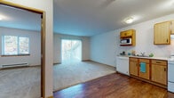 This single-floor unit offers a practical and comfortable layout designed for everyday living. The open-plan living and dining area features a combination of rich hardwood-style flooring and plush carpeting, creating a warm and inviting atmosphere. A large sliding glass door floods the living space with natural light and provides access to an outdoor area, framed by vertical blinds for privacy.

The kitchen is thoughtfully designed with warm oak cabinetry, white appliances including a range, dishwasher, refrigerator, and an over-cabinet microwave. A dedicated laundry closet is conveniently located just off the kitchen, housing a stacked washer and dryer unit. The kitchen flows seamlessly into the main living area, making the space feel open and connected.

The bedroom is a quiet, carpeted retreat with a wide window that brings in natural light and outdoor views, complemented by a baseboard heater for year-round comfort. The full bathroom features hardwood-style flooring, a vanity with cabinet storage, a full tub and shower combination, and accessibility-friendly grab bars — a practical and considerate design touch.

Throughout the unit, clean white walls, consistent trim work, and flush-mount lighting contribute to a tidy, neutral aesthetic that is easy to personalize.