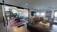 Located at 2501 Via Romana in Fort Worth, Texas, this thoughtfully designed single-story space blends contemporary aesthetics with warm, inviting elements across several distinct areas. Large-format tile flooring flows throughout, creating a cohesive foundation that unifies the layout.

The main lounge area is anchored by a plush leather sofa, a cushioned ottoman, and a sculptural velvet accent chair, all arranged around a wall-mounted flat-screen television. A richly textured wood credenza serves as a media console beneath the TV, while black-framed windows frame views of the surrounding exterior. Recessed lighting provides a clean, modern illumination throughout.

Adjacent to the lounge, a glass-walled game room houses a billiard table set atop a bold Persian-style area rug, lending warmth and color to the space. Floor-to-ceiling glass panels and expansive windows fill the room with natural light and offer visibility into an outdoor seating area.

A separate meeting or dining area features two solid wood communal tables paired with navy blue leather chairs with brass legs. Wainscoting in a muted blue-gray tone lines the walls, complemented by elegant brass wall sconces and framed artwork.

A connecting corridor features exposed brick accents, curated wall art, and glass-panel doors, adding an industrial yet refined character that ties the entire space together.