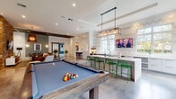 Located at 219 Depot Ave in Delray Beach, Florida, this single-floor amenity clubhouse delivers a vibrant, contemporary design tailored for socializing and productivity. Polished concrete floors run throughout, unifying each distinct zone within the open-concept layout. The entry area welcomes visitors with exposed beam accents, potted greenery, a reception counter with a stacked-stone backdrop, and sliding barn doors that add a touch of industrial charm.

The game and social lounge is a standout, featuring a billiard table, a seating cluster with mid-century-style wooden chairs, and French doors that invite abundant natural light and outdoor views. Adjacent to it, a fully equipped wet bar and entertaining kitchen showcases bold chevron-patterned wallcovering, white quartz countertops, stainless steel beverage refrigerators, a popcorn machine, vibrant green bar stools, and a mounted flat-screen TV — ideal for gatherings.

A cozy lounge area centers around a dramatic exposed brick accent wall with a mounted TV, plush sectional seating, and layered pendant lighting. A café-style dining nook offers banquette seating, marble-top tables, and curated artwork beneath tall windows. A dedicated business center provides workstations against a whitewashed brick wall, while a secondary flex room with bright green cabinetry and wall-mounted shelving completes the space.
