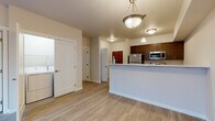 Located at 1403 South Assembly Street in Spokane, Washington, Unit A403 is a thoughtfully designed single-floor residence that combines modern finishes with a functional open layout. The kitchen is a standout feature, equipped with rich dark-walnut cabinetry, stainless steel appliances including a refrigerator, range, microwave, and dishwasher, and a sleek white countertop peninsula that doubles as a breakfast bar. Pendant lighting above the peninsula adds warmth and visual interest to the space. Light-toned luxury vinyl plank flooring runs throughout the main living and kitchen areas, lending a clean and cohesive look. The open-concept living area is generously proportioned, offering a bright and airy atmosphere enhanced by a sliding glass door that leads to a private balcony with outdoor views. The bedroom features plush carpeting and its own exterior door access to a balcony area. A dedicated laundry area with in-unit washer and dryer hookups adds everyday convenience. The bathroom is finished with light vinyl flooring, neutral tones, and a baseboard heating system. Wall-mounted heating and cooling units are present throughout, ensuring year-round comfort. The overall ambiance is clean, modern, and move-in ready.