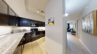 Located at 6975 Sierra Club Cir in Naples, Florida, this single-floor residence offers a thoughtfully designed layout with a cohesive, contemporary aesthetic throughout. The kitchen is a standout feature, showcasing rich dark cabinetry, granite countertops, a mosaic tile backsplash, and black appliances, all set atop light ceramic tile flooring. A pass-through opening connects the kitchen seamlessly to the dining area, which accommodates a round dining table and provides a welcoming space for meals. The living room is bathed in natural light from large windows dressed with navy drapes, offering outdoor views and a bright, airy atmosphere. A ceiling fan adds comfort, and a private door provides additional access to the exterior. Two well-proportioned bedrooms feature plush carpeting, ceiling fans, and ample natural light. The primary bedroom includes a walk-in closet and a serene color palette, while the second bedroom offers generous storage. Both bathrooms are finished with granite-topped dark vanities and tile flooring; one includes a tub-shower combination. Light tile flooring flows consistently through the main living areas, unifying the open floor plan and enhancing the overall sense of space throughout this Naples residence.
