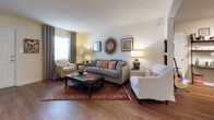 Located at 1870 Enterprise Drive in Virginia Beach, Virginia, this single-floor residence offers a functional and comfortable layout across several well-appointed rooms. The living area features warm wood-style flooring, natural light from a large window dressed with decorative curtains, and ample space for seating arrangements. A sunburst mirror and tasteful wall art add character to the room's inviting ambiance.

The kitchen is outfitted with honey-toned wood cabinetry, granite-style countertops, and black appliances including a range, microwave, dishwasher, and refrigerator. A window above the sink brings in natural light, and a stacked washer and dryer unit is conveniently accessible nearby.

The primary bedroom features plush carpeting, a large window with decorative curtain panels, and generous space for a full dresser and nightstands. A second bedroom carries a playful nautical theme, complete with fish and life ring wall decor, carpet flooring, and a dedicated study area. Both bedrooms are well-sized and offer natural light.

Two full bathrooms each include a shower-tub combination. Additional storage space is available, as evidenced by a dedicated nook with wood-style flooring. The entry area provides a welcoming foyer with hardwood-style floors and coastal-inspired artwork, setting the tone for the home's relaxed, beach-influenced aesthetic.