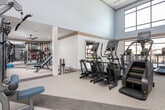 Located at 3196 US-280 E in Birmingham, Alabama, this single-story fitness center is designed to support a comprehensive range of workout routines. The main exercise floor is defined by soaring double-height ceilings and expansive floor-to-ceiling windows that flood the space with natural light while offering views of the surrounding outdoor greenery. Neutral-toned walls, wood accent beams, and a combination of carpet and hard flooring contribute to a clean, modern aesthetic throughout.

The primary cardio and strength area houses a robust selection of Matrix ellipticals, stair climbers, treadmills, and selectorized weight machines arranged for easy navigation. Full-length mirrors line sections of the walls, enhancing the sense of openness. A dedicated functional training zone features a multi-use cable and suspension rig stocked with medicine balls, kettlebells, resistance bands, and TRX straps, ideal for dynamic and sport-specific training.

A separate spin studio accommodates multiple Peloton-style stationary bikes and is lined with mirrors on one wall. Notably, this studio features a retractable glass garage door that opens directly to the outdoors, allowing fresh air and natural light to enhance indoor cycling sessions. Warm wood flooring and recessed lighting complete this room's inviting atmosphere.