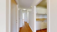Located in View Royal, BC, this single-floor, 2-bedroom, 1-bathroom residence offers a clean, functional layout with consistent warm-toned hardwood flooring throughout. The open living area is bright and spacious, featuring white walls and a straightforward design that maximizes usable space. A pass-through opening connects the living area to the kitchen, which is equipped with white cabinetry, light countertops, and built-in appliances including a dishwasher. A central hallway, accented with crown moulding, connects the main living areas to the bedrooms and bathroom. The primary bedroom is a comfortable size and features a large picture window that frames views of mature trees and greenery, filling the room with natural light. Both bedrooms include built-in closets with full-width rods for ample storage. The bathroom is finished with a white vanity, a marble-toned countertop, an undermount sink, and a mirrored medicine cabinet. An additional linen closet with built-in shelving is conveniently located adjacent to the bathroom. The unit also benefits from stair access visible in the dollhouse view, and baseboard heating throughout. The overall aesthetic is clean and neutral, offering a versatile canvas for personalization.