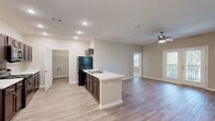 Located at 801 Booth Rd in Warner Robins, Georgia, this single-story home offers five bedrooms and three bathrooms across a thoughtfully designed floor plan. The open-concept kitchen and living area serves as the heart of the home, featuring rich dark cabinetry, white countertops, a center island with a sink, and black appliances including a refrigerator, range, and microwave. Recessed lighting and a ceiling fan with light kit keep the shared living space bright and comfortable. Wood-look luxury vinyl plank flooring flows throughout the main living areas, while plush carpeting adds warmth to the bedrooms. The bedrooms are well-proportioned, each with ceiling fans and ample natural light from windows with blinds that offer outdoor views of the surrounding greenery. A walk-in closet with wire shelving provides generous storage in the primary suite. The three bathrooms are finished with wood-look flooring, dark vanities, and full tub-shower combinations equipped with grab bars. A dedicated laundry room adds everyday convenience. A glass door in the living area opens to an outdoor area, further enhancing the home's connection to its surroundings. The neutral color palette and clean finishes throughout create a fresh, move-in-ready atmosphere.