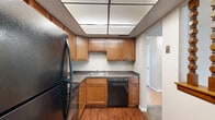 Located at 4285 Chestnut Ridge Road in Buffalo, NY, this one-bedroom, one-bathroom unit offers a practical and well-organized layout across a single floor. The living room is a comfortable, carpeted space highlighted by a large sliding glass door fitted with vertical blinds, allowing natural light to fill the room and providing outdoor access. The kitchen features warm-toned wood cabinetry, granite-style countertops, hardwood flooring, and a full suite of black appliances including a refrigerator, dishwasher, and range. A distinctive drop ceiling with recessed panel lighting adds a functional, finished look to the kitchen area. A hallway connects the main living spaces to the bedroom and bathroom, with light hardwood flooring providing a clean transition. The bedroom is a generously proportioned, carpeted room featuring a wide window that brings in natural light and a built-in closet offering ample storage. The bathroom is clean and straightforward, equipped with a full tub-shower combination with a white surround, a vanity with mirror, and tile flooring. Throughout the unit, neutral wall tones and textured ceilings contribute to a consistent, understated aesthetic.