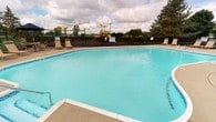 This single-floor community facility offers a well-rounded combination of recreational and operational spaces designed to support both residents and staff. At the heart of the outdoor amenities is a generously sized swimming pool with clear, inviting turquoise water, surrounded by a concrete pool deck with lounge seating. A safety fence encloses the area, and a colorful playground structure is visible in the background, set against a backdrop of mature trees and open sky.

Inside, the facility includes a dedicated back-office and storage area that serves the operational needs of the property. The storage room features wall-mounted shelving units stocked with labeled document boxes, reams of copy paper, folding chairs, and various supplies — reflecting an organized system for managing community records and materials. A clothing rack holds staff garments alongside miscellaneous equipment, including cleaning tools and safety signage. Filing cabinets and posted compliance documentation indicate an active administrative function. The interior doors are finished with classic white paneled millwork and brass hardware, adding a clean, traditional touch to the utilitarian spaces. Together, these areas reflect a fully functioning community hub designed to serve both day-to-day operations and the recreational needs of its users.