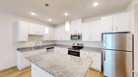 Located at 691 Union Chapel Rd in Cedar Creek, TX, this single-story home offers a thoughtfully designed layout with three bedrooms, two bathrooms, a closet, and a combined kitchen and living area. The kitchen is a standout feature, showcasing crisp white shaker cabinetry, granite countertops with a subtle speckled pattern, a large center island, and a full suite of stainless steel appliances including a range, microwave, dishwasher, and refrigerator. Pendant lighting and recessed fixtures illuminate the space with a clean, modern feel. Light hardwood-style flooring runs throughout the main living areas and kitchen, lending warmth and continuity. The living room benefits from multiple windows dressed with white horizontal blinds, allowing natural light to fill the open space. The bedrooms feature plush carpeting, ceiling fans, and windows that bring in additional natural light. The primary bedroom is generously sized with direct access to a bathroom featuring granite-topped white cabinetry and a large mirror. The second bathroom mirrors the same refined finishes, with white cabinetry, granite counters, a tub-shower combo, and hardwood-style flooring. Neutral walls and clean architectural lines throughout the home create a bright, versatile ambiance suitable for a variety of living styles.