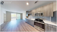 This one-bedroom, one-bathroom unit in Raleigh, NC offers a thoughtfully designed, modern interior with a cohesive neutral palette and light-toned luxury vinyl plank flooring carried throughout. The open-concept kitchen and living area forms the heart of the unit, where a contemporary kitchen showcases wood-grain cabinetry extending to the ceiling, light-colored quartz countertops, a subway tile backsplash in soft blue-gray, and a full suite of stainless steel appliances including a range, over-the-range microwave, dishwasher, and refrigerator. The living area flows directly from the kitchen and features a sliding glass door with vertical blinds, opening to a private balcony with outdoor views.

The spacious primary bedroom offers ample room, a ceiling fan, and large windows that bring in generous natural light and tree-lined views. The bathroom is well-appointed with wood-grain vanity cabinetry, wood-look flooring, and a full-size walk-in shower enclosed by a sleek frameless sliding glass door with floor-to-ceiling tile surround. A dedicated laundry area houses a stacked washer and dryer unit, adding everyday convenience. Clean lines, recessed lighting, and a bright, neutral finish give the space a fresh, modern character throughout.