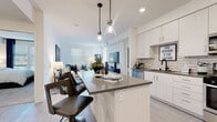Located at 1575 Camino Altezza in Chula Vista, CA, this single-floor residence offers a thoughtfully designed open-concept layout that seamlessly connects the kitchen, dining, and living areas. The kitchen is outfitted with crisp white cabinetry, grey quartz-style countertops, a classic subway tile backsplash, and stainless steel appliances including a gas range, over-the-range microwave, and refrigerator. A central island with bar seating and pendant lighting adds both functionality and style. Light wood-style flooring runs throughout the main living areas, enhancing the bright, airy atmosphere created by an abundance of natural light from multiple windows. The living room is a welcoming space with room for generous seating arrangements and a calm, neutral aesthetic. The bedroom is carpeted and well-lit by large windows, offering a serene retreat, and is complemented by a spacious walk-in closet with wire shelving for ample storage. The bathrooms feature a consistent design language — white cabinetry, grey countertops, tile-surround soaking tubs, and wood-look tile flooring — presenting a clean, modern finish throughout. The overall design balances contemporary style with comfortable, functional living.