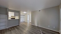 This single-floor residence offers a practical and well-maintained layout designed for comfortable everyday living. The open living area is finished with durable wood-style flooring in a warm gray tone that extends throughout the space, complemented by neutral warm-beige walls and a textured ceiling. The living area flows naturally toward a walk-in closet and a full bathroom, keeping daily functions conveniently accessible. A half-wall partition separates the living space from the galley-style kitchen, which features white cabinetry extending to the ceiling, a light stone-finish countertop with a stainless steel sink, a white refrigerator, and a coil-burner electric range — all arranged efficiently along parallel walls. The bedroom is bright and airy, highlighted by a ceiling fan with a light fixture, vertical blinds covering a large sliding glass door that invites natural light, and access to the adjoining bathroom. The bathroom is clean and functional, equipped with a white vanity topped with a stone-finish surface, a large mirror, and brushed nickel hardware and fixtures. Throughout the residence, consistent flooring, neutral tones, and well-placed ventilation create a cohesive, move-in-ready environment.
