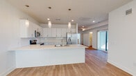 This single-floor residence showcases a clean, contemporary design with a cohesive neutral palette throughout. The open-concept kitchen serves as the centerpiece of the main living area, featuring white shaker-style cabinetry extending to the upper walls, a white subway tile backsplash, and a large waterfall-edge island with an integrated sink. Stainless steel appliances — including a French door refrigerator with ice and water dispenser, electric range with over-the-range microwave, and dishwasher — provide a polished, modern finish. Pendant lighting hangs above the island, complementing recessed ceiling lights. Light hardwood-style flooring flows through the kitchen and living areas, creating a bright, open atmosphere. A sliding glass door connects the main living space to an outdoor area, allowing natural light to filter in.

The bedrooms feature plush carpet flooring and clean white walls, offering a calm and versatile canvas. The bathrooms are finished with white cabinetry, light countertops, hardwood-style flooring, and tub-shower combinations with curved chrome curtain rods. A dedicated laundry area includes a full-size washer and dryer alongside a large closet with wire shelving. Carpeted stairs provide access to an additional level above.