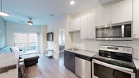 Located at 300 W State St in West Lafayette, Indiana, this thoughtfully designed unit offers four bedrooms and three bathrooms across a single floor. The open-concept kitchen and living area serves as the heart of the space, featuring stainless steel appliances — including a range, microwave, and dishwasher — paired with two-tone cabinetry in white and dark wood finishes, a white subway tile backsplash, and a stainless steel sink. Wood-style flooring runs throughout, adding warmth and visual continuity. The living area is bright and welcoming, with a sliding glass door that opens onto a private balcony, providing outdoor views and natural light. Each bedroom is efficiently designed with ceiling fans and windows that bring in daylight. The primary bedroom includes a dedicated walk-in closet fitted with built-in shelving and a dresser. The bathrooms are finished with classic penny-tile flooring, subway tile shower surrounds, dark-toned vanities, and framed mirrors, offering a clean and contemporary aesthetic. The overall design balances modern finishes with functional layouts, making this a well-appointed unit ideal for shared living in the heart of West Lafayette.