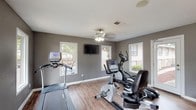 Located at 2144 Lakeshore Dr in Ridgeland, Mississippi, this single-floor fitness center is a well-equipped space designed to support a range of cardio-focused workouts. The room is finished with warm hardwood-style flooring that contrasts neatly against the cool gray walls and crisp white baseboards, creating a clean and functional aesthetic throughout.

The space is outfitted with a comprehensive selection of cardio equipment, including a treadmill, elliptical trainer, upright stationary bike, and a recumbent exercise bike, offering users a variety of workout options. A wall-mounted flat-screen television is positioned for easy viewing during exercise, and a ceiling fan with a light fixture provides both air circulation and ambient lighting.

Multiple windows line the walls, allowing generous natural light to fill the room while offering views of the surrounding outdoor greenery. A water cooler station is conveniently available, ensuring hydration is within easy reach. The space also features a posted fitness rules or cardio notes board, indicating an organized and community-oriented environment. Access to the outdoors is provided through a glass-panel door, further enhancing the bright and open feel of the facility.