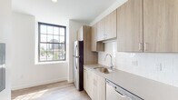 Located at 1 Atlantic St in the heart of downtown Stamford, Connecticut, this modern single-floor unit combines contemporary design with functional living. The space is finished with light wood-tone flooring throughout the main living and bedroom areas, creating a warm and cohesive aesthetic against crisp white walls.

The galley-style kitchen is well-appointed with light wood cabinetry, a subway tile backsplash, quartz-style countertops, and a full suite of stainless steel appliances including a refrigerator, electric range, microwave, and dishwasher. A single-basin stainless steel sink with a modern arc faucet completes the kitchen setup.

The living and bedroom areas benefit from large, multi-pane windows with dark frames that flood the space with natural light while offering elevated views of the surrounding Stamford cityscape and streetscape below. The open, bright interiors create an airy feel throughout.

The bathroom features large-format tile flooring in a neutral stone-like finish, paired with clean white walls and fixtures. A spacious layout includes a shower area, toilet, and vanity with coordinating wood-tone cabinetry. The unit's overall design reflects a clean, modern aesthetic well-suited for urban living in one of Connecticut's most vibrant city centers.
