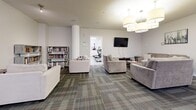 This single-floor amenity space in California offers a comprehensive set of facilities designed to support both active and social pursuits. The layout is divided into two primary areas that flow seamlessly into one another.

The fitness center is a bright, generously sized area finished with durable speckled flooring and clean white walls accented by a bold yellow feature wall. It is well-lit by overhead fluorescent lighting and equipped with a variety of cardio machines including treadmills, ellipticals, and a stationary bike, alongside a multi-station strength training unit. A wall-mounted television, stability balls, and motivational fitness artwork complete the space.

The adjacent community room is a versatile, carpeted space with patterned tile-style carpet in neutral tones with red accents. It features a comfortable lounge area with plush sofas, a flat-screen television, and a bookshelf stocked with reading material. A large conference-style table with multiple chairs accommodates meetings or group gatherings, while a pool table adds a recreational element. Structural columns punctuate the space, and recessed and pendant lighting provide a warm, inviting ambiance. Together, these areas form a functional and welcoming amenity hub suited for fitness, relaxation, and community engagement.