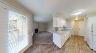 This single-floor residence offers a practical and well-organized layout that balances comfort with functionality. The living area is a generously sized, carpeted space anchored by a fireplace with a clean white mantel and tile surround, creating a welcoming focal point. Natural light enters through blinded windows, and a ceiling fan adds to the room's comfort. The kitchen is designed in a galley style, featuring white cabinetry — both upper and lower — with brushed nickel hardware, light countertops, a built-in sink, a white electric range, and a refrigerator. Wood-look vinyl flooring runs throughout the kitchen and entry corridor, providing a durable, easy-to-maintain surface. A peninsula counter connects the kitchen to the living area, offering an open, communicative flow between the two spaces. The bedrooms are carpeted and neutrally toned, each equipped with closets — one featuring mirrored sliding doors and another with a standard reach-in design. Windows in the bedrooms allow for natural light and outdoor views. The bathroom is clean and efficiently laid out, with white cabinetry, a single-basin vanity, and a full-size soaking tub and shower combination, all complemented by wood-look flooring.