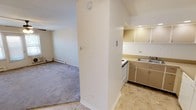 This single-floor residence offers a practical and functional layout designed for comfortable everyday living. The living area is generously sized, featuring soft wall-to-wall carpeting, a ceiling fan with integrated lighting, and baseboard heating throughout. Large windows and a set of glass-paneled doors allow natural light to fill the space, creating a bright and open atmosphere. The room flows naturally toward the kitchen, which is separated by a partial wall divider. The kitchen is outfitted with a U-shaped layout, offering ample upper and lower cabinetry in a warm neutral tone, recessed lighting, white tile backsplash, a double-basin sink, and stone-look tile flooring. White appliances, including a refrigerator and dishwasher, complete the space. The bedrooms are well-proportioned, each featuring carpeted floors, ceiling fans, and baseboard heaters. One bedroom benefits from a window that brings in natural light, while another includes a built-in closet with shelving for added storage. The bathroom is clean and bright, finished with marble-look tile flooring, a full soaking tub with shower, a vanity sink, and a small window for natural ventilation. The unit presents a straightforward and livable floor plan throughout.