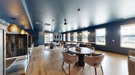 Located at 808 Melvin Ct in Madison, WI, this single-floor community lounge offers a well-appointed, thoughtfully designed gathering space. The interior is defined by a cohesive color palette of deep navy and steel blue walls paired with warm light wood flooring, creating a sophisticated yet inviting atmosphere throughout.

The main living area serves as the social hub, featuring multiple round tables with upholstered chairs arranged on textured area rugs, providing flexible seating for casual gatherings or conversation. A dedicated lounge zone offers comfortable armchairs, a wall-mounted TV, and large windows that flood the space with natural light and provide views to the outdoors.

Along one wall, a striking geometric-patterned accent wall in blue and white sets the backdrop for a row of intimate banquette booths with plush cushioned seating and warm amber pendant lighting overhead — ideal for smaller group settings. A service bar area with decorative pendant lights and tiled backsplash anchors one end of the space.

A private meeting or conference nook features distinctive patterned wallpaper, soft mint-green wainscoting, a round table, and leather seating, offering a quieter retreat within the larger layout. The deep blue ceiling treatment adds depth and visual continuity across all areas, tying the design together with a polished, modern aesthetic.
