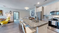 Located in Houston, TX, this well-appointed 2-bedroom, 2-bathroom residence offers a thoughtfully designed open-concept layout across a single floor. The kitchen is a standout feature, showcasing a large granite-topped island with bar seating, light wood cabinetry, a full suite of stainless steel appliances including a French door refrigerator, microwave, and range, plus a tile backsplash — all flowing seamlessly into the living area. The living room is bright and welcoming, with wood-style plank flooring, a ceiling fan, and a door providing access to natural light from outside. The spacious primary bedroom features plush carpet, a ceiling fan, and direct access to a walk-in closet with wire shelving. The second bedroom is equally comfortable with similar finishes. Both bathrooms are finished with granite vanity tops, wood-tone cabinetry, and tile-surround tub/shower combinations with light plank flooring. A dedicated in-unit laundry room accommodates a full-size washer and dryer with additional wire shelving for storage. The overall aesthetic is clean and contemporary, with a neutral color palette and modern finishes throughout.