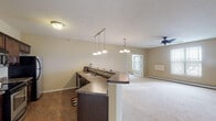 Located at 1210 Seventh Ave S in Sartell, Minnesota, this single-floor unit offers a thoughtfully designed open-concept layout that connects the kitchen and living areas seamlessly. The kitchen is equipped with stainless steel appliances, including a refrigerator, range, and microwave, complemented by rich dark wood cabinetry and granite-style countertops. A wraparound breakfast bar with pendant lighting serves as a functional divider between the kitchen and the expansive carpeted living area. Tile flooring runs through the kitchen, providing a clean contrast to the soft carpet found throughout the rest of the unit.

The living area is generously proportioned, featuring a ceiling fan, baseboard heating, and large windows that allow natural light to fill the space. Bedrooms are carpeted and well-lit by natural light through windows fitted with blinds, offering exterior views. A spacious walk-in closet with wire shelving provides ample storage. The bathroom features tile flooring, a dark wood vanity with a white countertop, and a shower-tub combination. Neutral warm-toned walls throughout the unit create a cohesive and inviting ambiance.