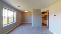 This single-floor unit offers a practical and well-organized layout connecting the main living spaces in a cohesive flow. The living area is generously proportioned, featuring neutral gray walls, light-toned hard-surface flooring, and a textured ceiling. A window along one wall allows natural light to filter in, while a thermostat and multiple electrical outlets add everyday convenience. The space opens toward the kitchen, which is partially separated by a structural divider, creating a sense of definition without full enclosure.

The kitchen is equipped with stainless steel appliances, including a refrigerator and electric range, complemented by white cabinetry that extends to the upper walls for ample storage. Light-toned countertops and a single-basin sink complete the functional workspace, with warm hardwood-style flooring underfoot.

The bedrooms are carpeted in neutral tones, each featuring windows that introduce natural light and outdoor views of surrounding greenery. The rooms are well-proportioned with clean walls and textured ceilings consistent throughout the unit.

The bathroom includes a tiled tub-shower combination, a toilet, and hard-surface flooring, finished with chrome fixtures and towel bars. Overall, the unit maintains a clean, understated aesthetic suited for comfortable everyday living.