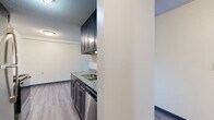 Located at 1902 Warren St. in Mankato, MN, this one-bedroom, one-bathroom unit offers a well-designed layout across a single floor. The galley-style kitchen is a standout feature, outfitted with dark cabinetry, granite-look countertops, a double-basin sink, and a full suite of stainless steel appliances including a refrigerator, range, microwave, and dishwasher. The kitchen connects seamlessly to a combined dining and living area, which benefits from a large window fitted with vertical blinds, allowing natural light to fill the space. Hardwood-style flooring runs throughout, complemented by dark baseboards that add a clean, modern contrast to the neutral white walls and textured ceilings. The spacious bedroom includes an open closet with a hanging rod, providing practical storage. A hallway leads to two closets for additional storage needs. The full bathroom features a matching dark vanity with granite-look countertops, a tub-shower combination, and hardwood-style flooring consistent with the rest of the unit. A baseboard heating system and wall-mounted air conditioning unit ensure year-round comfort in this efficiently arranged and thoughtfully finished space.
