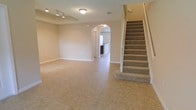 This two-story home offers a clean, functional layout designed for comfortable everyday living. The main level greets you with a generously sized open living area finished with neutral-toned ceramic tile flooring that runs throughout the common spaces, lending a cohesive and easy-to-maintain aesthetic. Soft, warm wall colors create an inviting and airy atmosphere, complemented by flush-mount and track lighting overhead that ensures the space is well illuminated.

A distinctive arched entryway connects the main living area to additional rooms beyond, including a glimpse of the kitchen featuring dark cabinetry in the background. This architectural detail adds a touch of elegance and visual interest to the otherwise clean-lined interior. A wide doorway nearby provides access to further spaces on the main floor.

The carpeted staircase, accented with crisp white railings and balusters, leads to the second floor, offering a comfortable transition between levels. The staircase is centrally positioned, making it both a practical and visually prominent feature of the main level.

Overall, the home presents a neutral, move-in-ready environment with a straightforward floor plan, consistent finishes, and a bright, open feel throughout both floors.