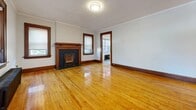 This well-appointed single-floor residence offers a thoughtful layout across one bedroom, one bathroom, and two living areas connected by hallways. The living room serves as the centerpiece of the home, highlighted by gleaming hardwood floors, crown molding, rich wood-trimmed windows and doorways, a textured ceiling, and a classic decorative fireplace with a black brick surround — adding warmth and vintage character to the space. A cast-iron radiator provides supplemental heating and contributes to the home's period charm. The secondary living area echoes this aesthetic with the same hardwood flooring, crown molding, and natural light from wood-framed windows. The kitchen has been modernized with white cabinetry, marble-patterned wall panels, hexagonal tile flooring, glass shelving, and a full suite of stainless steel appliances including a refrigerator, range, and dishwasher. The bedroom is a serene, light-filled space featuring hardwood floors, a window with outdoor views, and a cast-iron radiator. A dedicated closet with built-in hooks offers practical storage. The bathroom is finished with clean white subway tile walls, a full soaking tub, and a frosted window that allows natural light while maintaining privacy throughout.