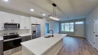This contemporary 1280 square foot residence in Elgin, Illinois offers a thoughtfully designed single-story layout. The home features three bedrooms, including a spacious 370 square foot primary suite, and two full bathrooms. The heart of the home is an open-concept living area that seamlessly combines the kitchen and living room, creating an ideal space for both everyday living and entertaining.

The kitchen is a standout feature, boasting sleek white cabinetry, stainless steel appliances, and a modern island with a built-in sink and ample seating. A striking linear chandelier adds a touch of sophistication to the space. Throughout the home, large windows allow natural light to flood the rooms, enhancing the bright and airy atmosphere.

The bedrooms are well-proportioned, with the primary bedroom offering generous space and likely an en-suite bathroom. The bathrooms feature contemporary fixtures and finishes, including a combination tub-shower in at least one.

Flooring varies throughout the home, with stylish wood-look flooring in the main living areas and kitchen, plush carpeting in some bedrooms, and durable concrete in utility spaces. The neutral color palette of whites and light grays provides a blank canvas for personalization.

Overall, this home presents a modern and efficient living space, ideal for those seeking contemporary comfort in a suburban setting.