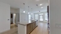This thoughtfully designed one-bedroom, one-bathroom unit offers a modern living experience with high-quality finishes throughout. The open-concept kitchen serves as the centerpiece of the living space, anchored by a large island with a striking granite countertop, an undermount sink, and stylish pendant lighting overhead. Taupe shaker-style cabinetry lines the kitchen walls, complemented by a white subway tile backsplash and a full suite of stainless steel appliances, including a refrigerator, range, and microwave. Light wood-tone flooring runs throughout the main living areas, adding warmth and continuity to the open layout. Multiple windows allow natural light to fill the space, while a ceiling fan serves the living area. The bedroom is carpeted for comfort, features two windows with blinds, and is served by a ceiling fan. It connects directly to the bathroom, which is finished with granite countertops, taupe cabinetry with brushed nickel hardware, and an undermount sink. A dedicated closet with rod and shelf storage adjoins the bathroom, providing practical organization. The clean, neutral color palette and consistent use of quality materials give this unit a cohesive, contemporary aesthetic throughout.