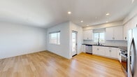 This well-designed 2-bedroom, 2-bathroom single-floor residence offers a clean, modern aesthetic throughout. The open-concept kitchen and living area serves as the heart of the home, featuring light hardwood flooring, recessed lighting, and an abundance of natural light from multiple windows. The kitchen is fully equipped with stainless steel appliances — including a refrigerator, range, over-the-range microwave, and dishwasher — complemented by crisp white shaker cabinets, dark countertops, and a white subway tile backsplash. A wall-mounted mini-split unit provides efficient climate control in the living area. Both bedrooms are carpeted and filled with natural light through large windows that frame outdoor views of the surrounding landscape. The primary bedroom is a comfortable size, while the second bedroom offers similar finishes and brightness. Each bathroom features a tub-shower combination finished with glossy white subway tile and matte black fixtures, creating a sharp, contemporary contrast. A dedicated closet provides additional storage. The unit's neutral white walls and consistent use of light materials throughout contribute to a cohesive, airy ambiance.